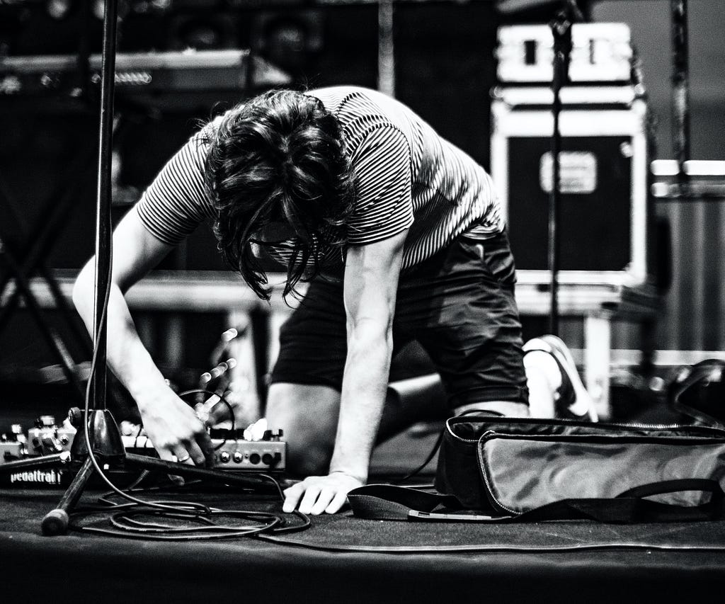 grayscale photography of man in striped shirt setting up equipment for a concert