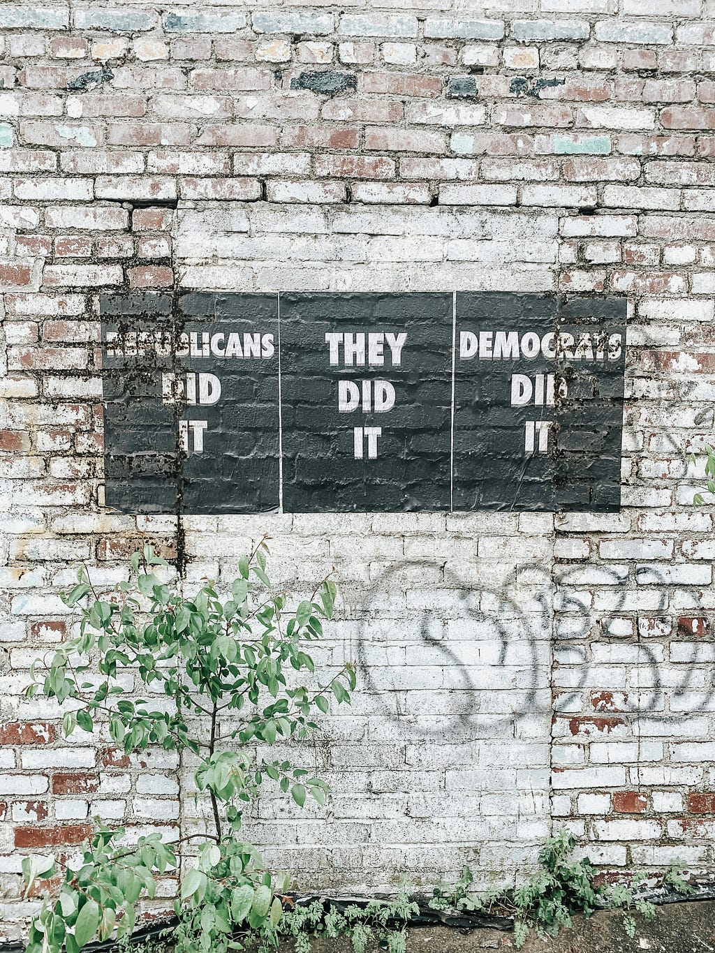 Brick wall with three black rectangles stating three opinions: REPUBLICANS DID IT; DEMOCRATS DID IT; THEY DID IT.