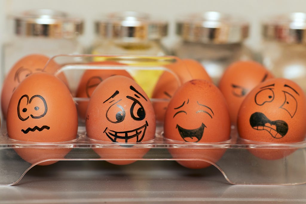 Picture shows an egg holder with 8 eggs, that all have faces drawn on them with a sharpie showing different emotions.