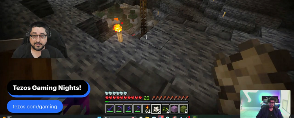 Minecraft livestream screenshot showing a player exploring a torchlit cave with scaffolding, flanked by two streamer webcam feeds, one of which shows AJ and the other Blangs.