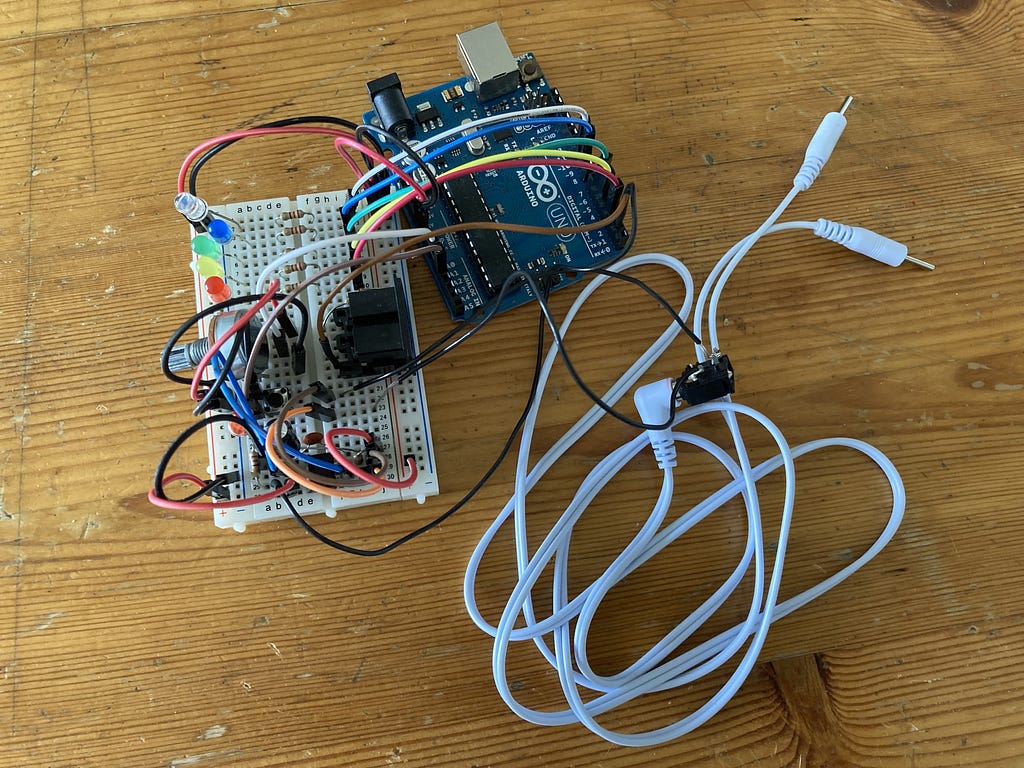 An Arduno Uno circuit board sits on a table connected with many colourful wires to a solderless breadboard containing electronic components including LEDs and resistors.