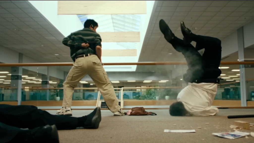 A screenshot from Everything Everywhere All At Once. Alpha-Waymond, a middle-aged asian man, stands over a security guard who is violenty faceplanting on the ground.