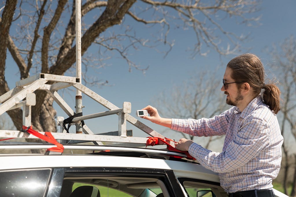 UT Assistant Professor Pawel Misztal stands next an SUV and adjusts the “Sniffer” instrumentation that sits on top of it.