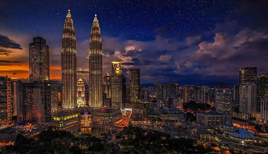 a photograph shows downtown kuala lumpur lit up during the dusk hours