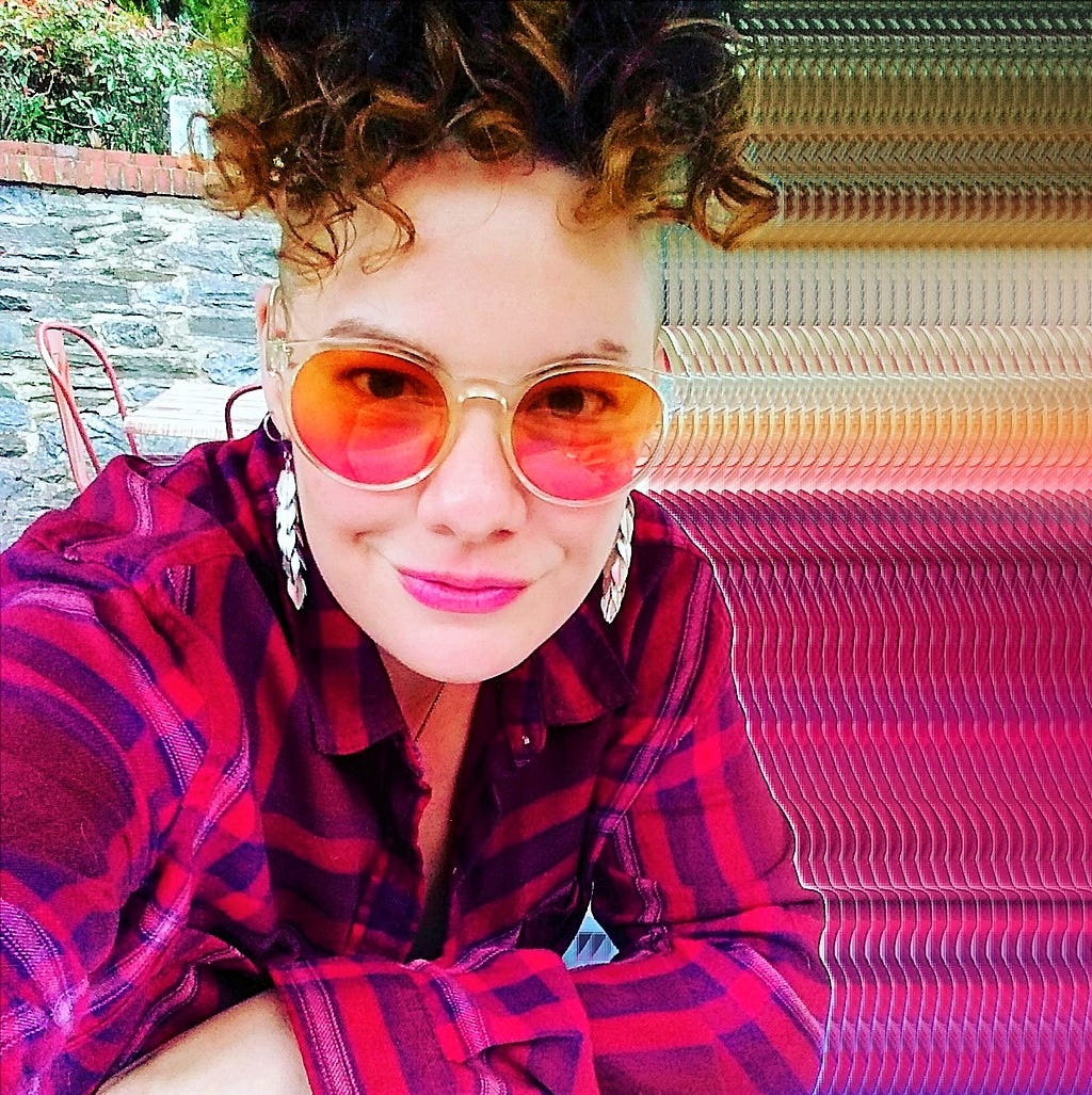 Colorful radiant author photo of Jessica McHugh wearing colorful sunglasses and with a curly hairstyle atop her head, pink flannel shirt, and dangly earrings.