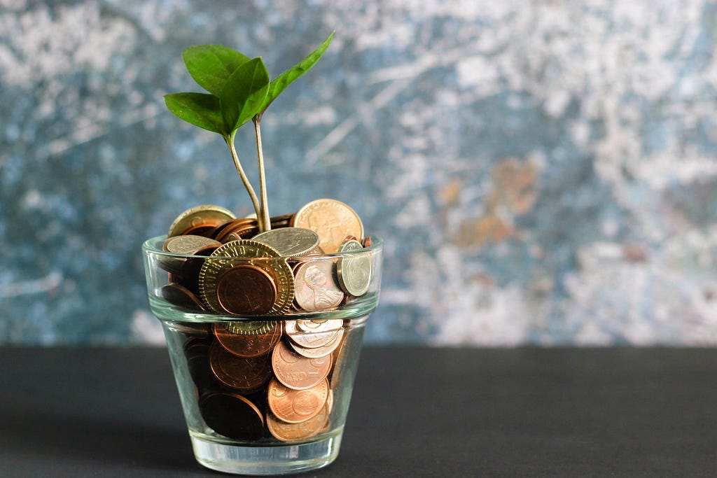 Glass of coins with a small plant growing out of it.