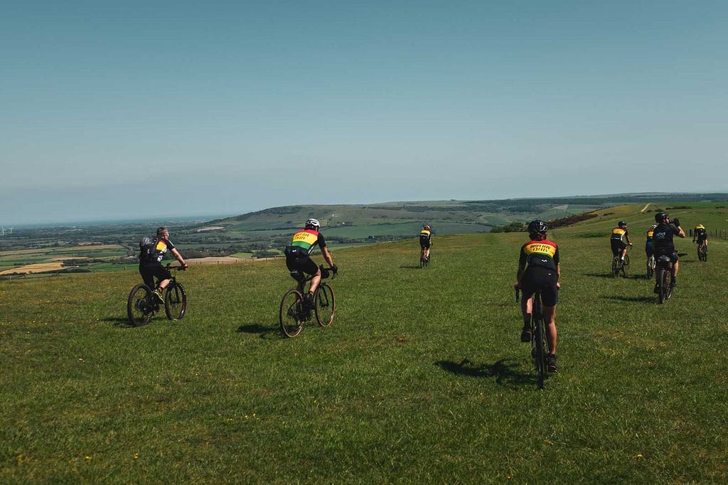 A group of cyclists in club kit on the grassy South Downs Way.