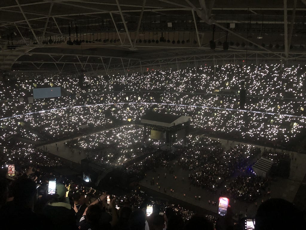 A photo of fans shining their phone torches amid total darkness inside the stadium.