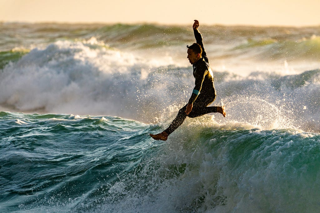 A surfer flies through the air above an ocean wavescape, his surfboard nowhere in sight