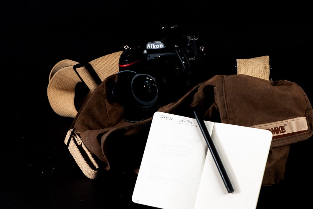 A display of a camera bag, camera with lens attached, and a pocket notebook with fountain pen for note taking duties. Oberhausen, Germany, September 24, 2022.