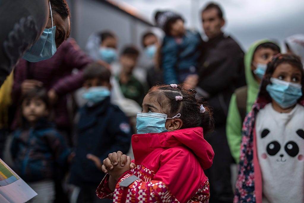 A young migrant girl in prayer, wearing a Covid-19 protection mask. (AP Photo/Petros Giannakouris)