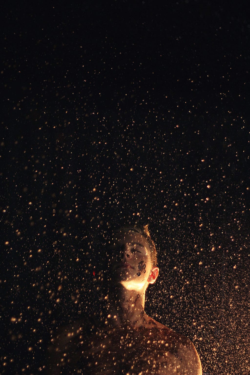 A person standing in front of a black background with gold flecks falling around them.