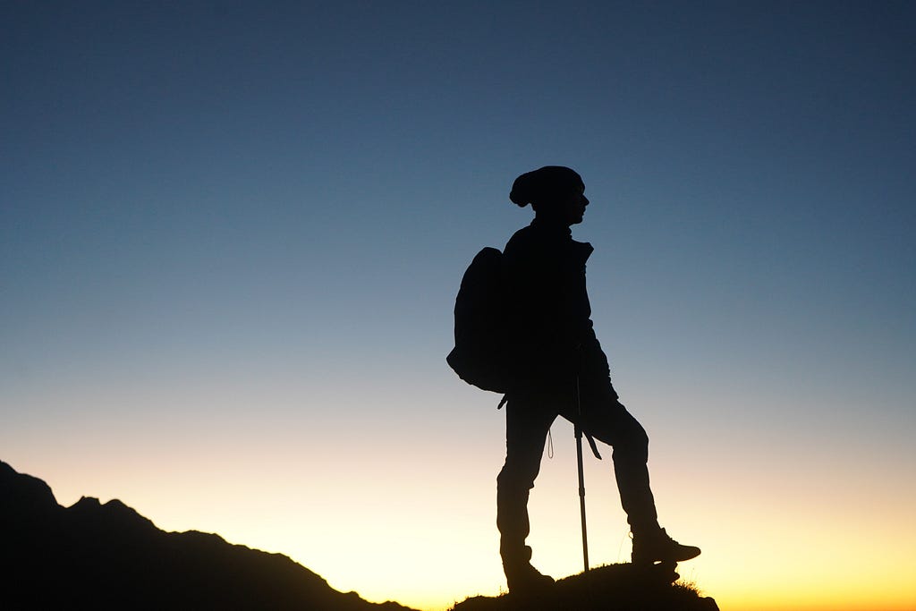 A travler/hiker standing at the corner of the top of the mountain depicting the notion of traveling causing sudden self realization or exploration of self.