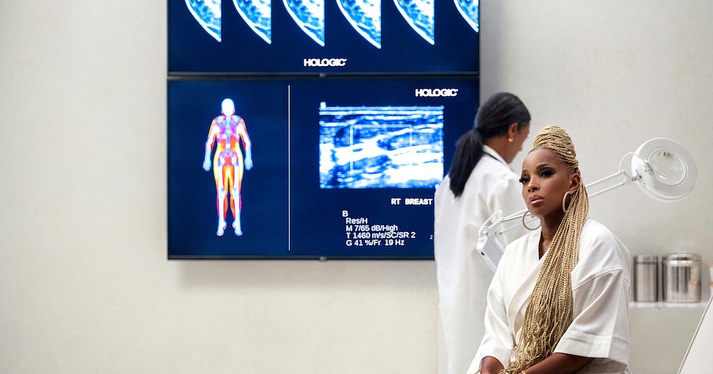 Photograph of a large doctor’s office with Mary J. Blige sitting in the foreground and body/breast imaging on the wall.