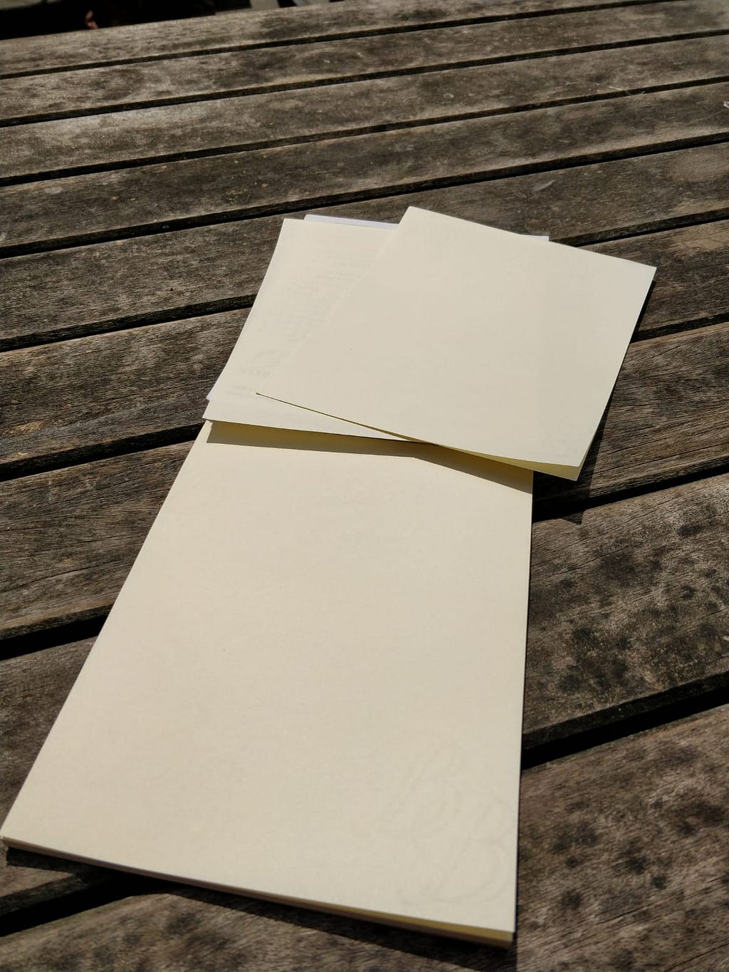 Two sheets of cream-coloured letter-writing paper on a wooden bench.