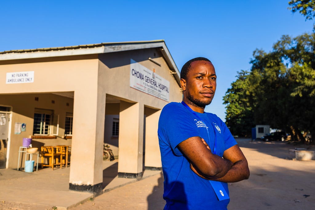 A young man with his arms crossed stands outside Choma General Hospital in Zambia.