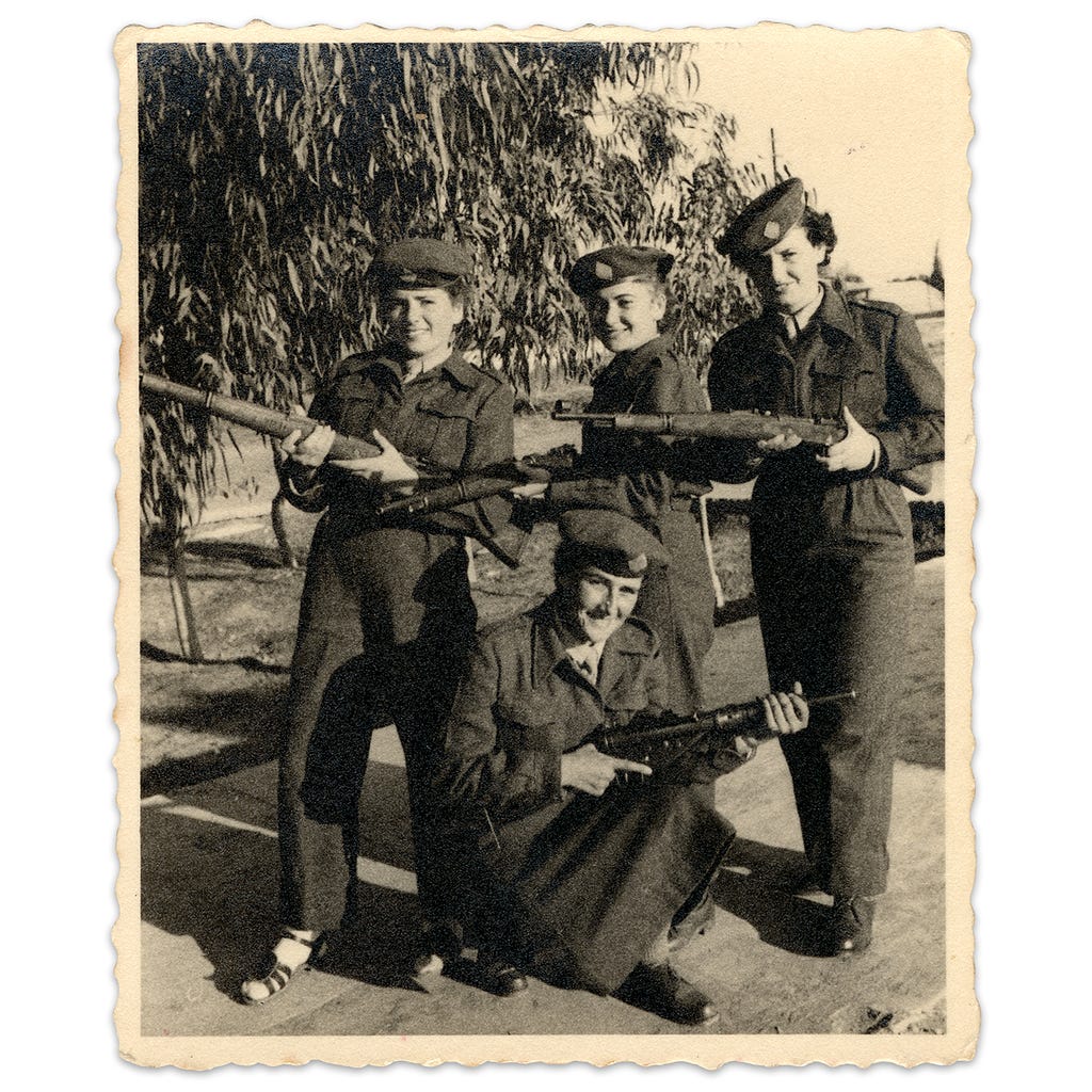 Four women wearing uniforms pose with guns on a sunny day.