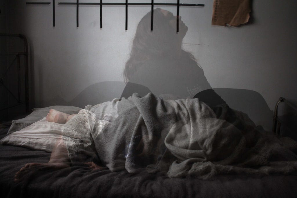 A bed with the blurry outlines of a person both lying down and sitting up in the bed, implying restless sleep.