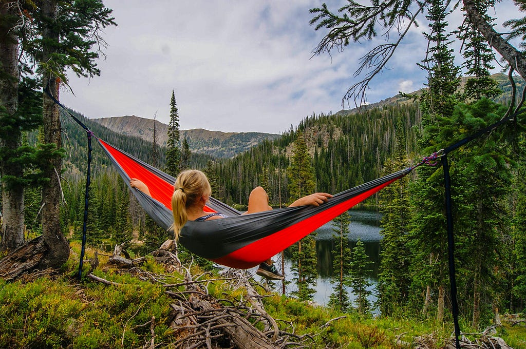 Woman relaxing in a vivid red hammock overlooking a scene of lush mountains, trees and a lake.