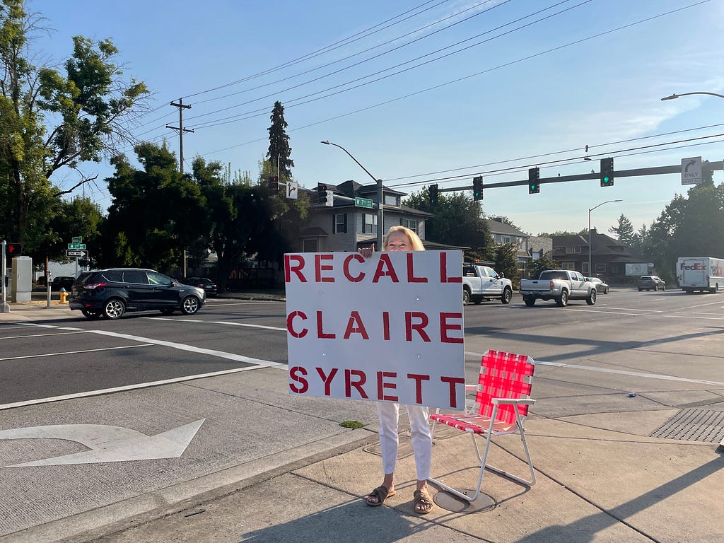 Meta Maxwell holds a “recall Claire Syrett” sign on the side of 7th Avenue in Eugene.