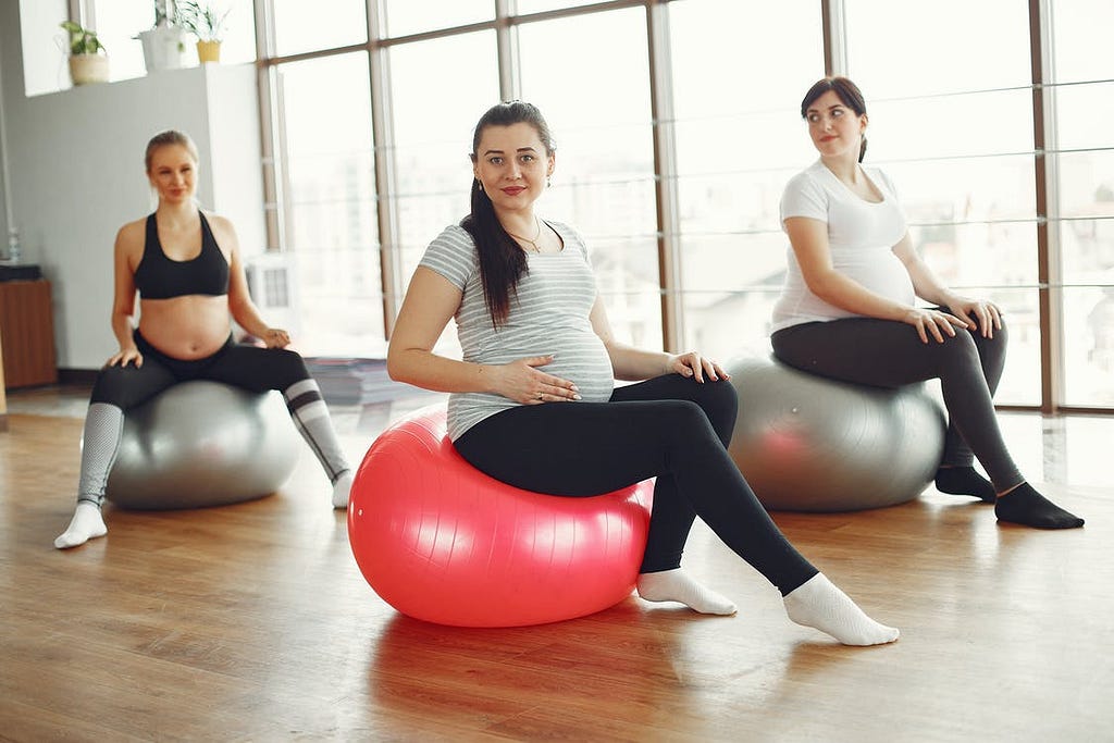 Three pregnant women seated on exercise balls for a yoga class.