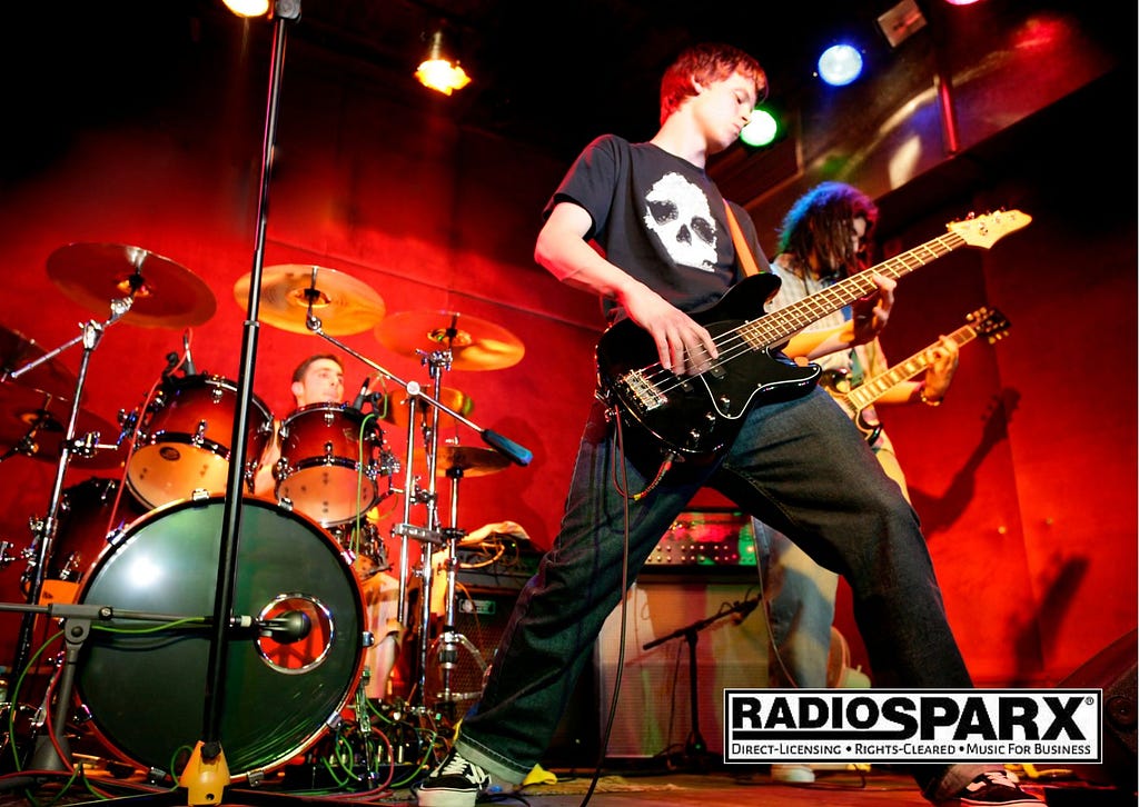 Young rock band with lead guitarist in full motion, playing for an audience.