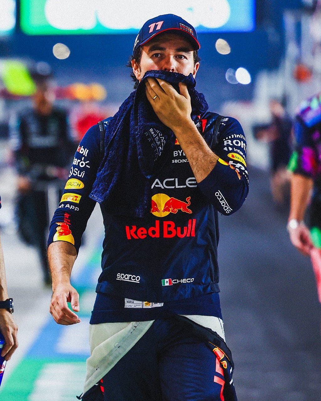 Checo walking with his race suit around his waist, wiping his face with a blue towel.