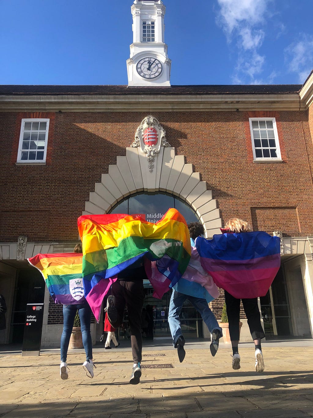 Students with LGBT+ pride flags jumping outside Middlesex University