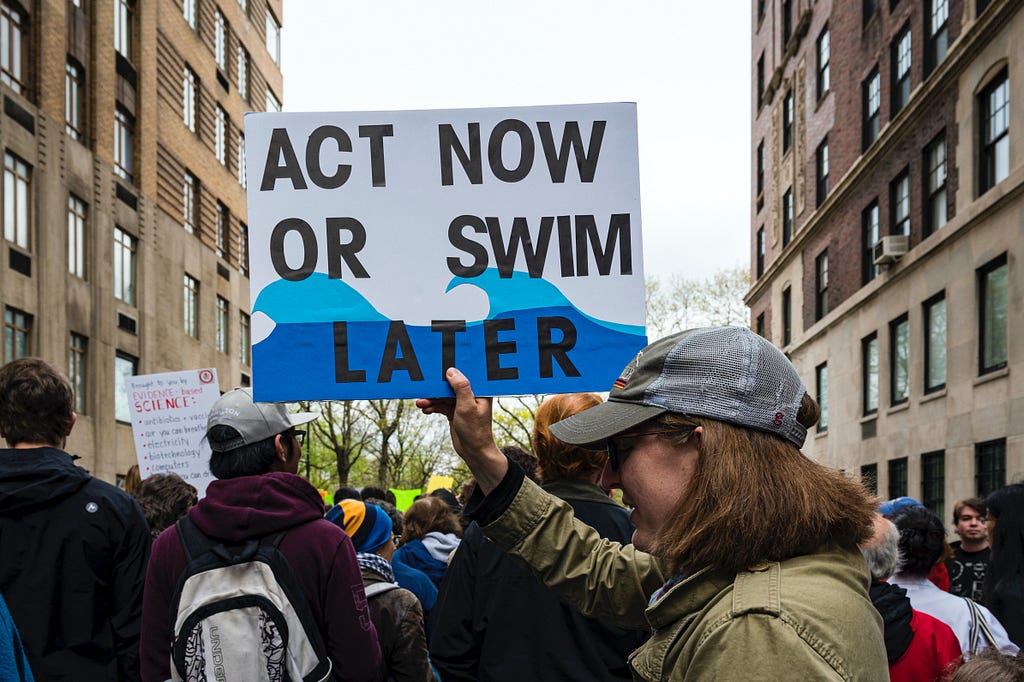 Protestor with sign that reads: “Act Now or Swim Later”