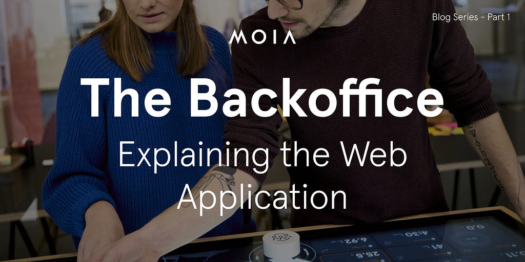 A woman and a man point to a display that shows some metrics. There is text added to the image, it reads: The Backoffice — Explaining the Web Application