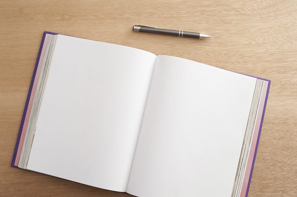 An open notebook with blank pages on a oakwood background. A black pan above the notebook.