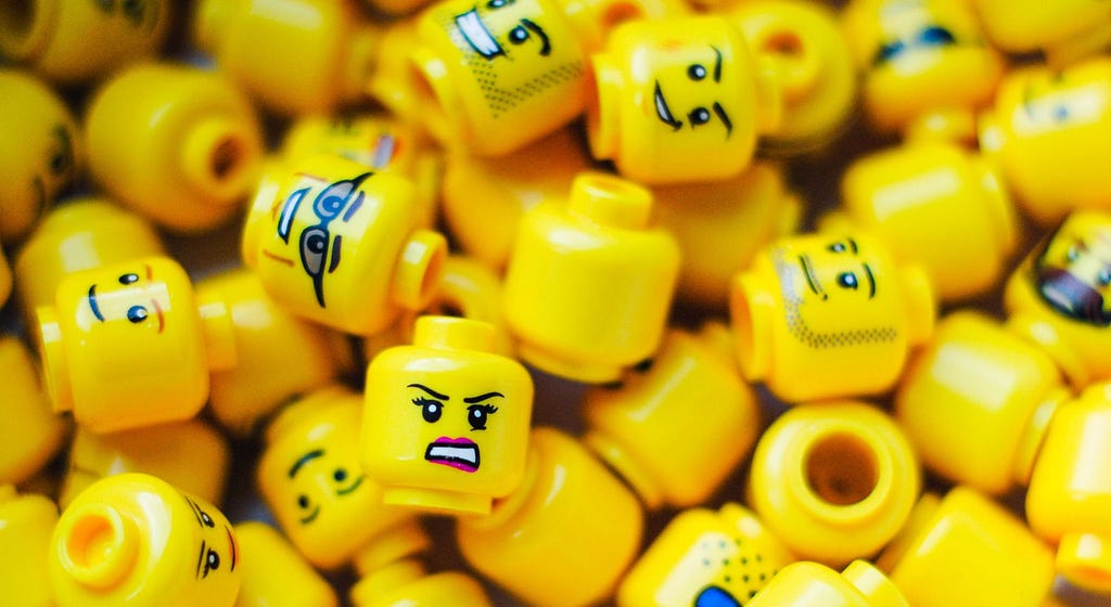 Imagem com várias peças de Lego em formato de cabeça representando várias emoções que remetem a felicidade, desgosto e tranquilidade.