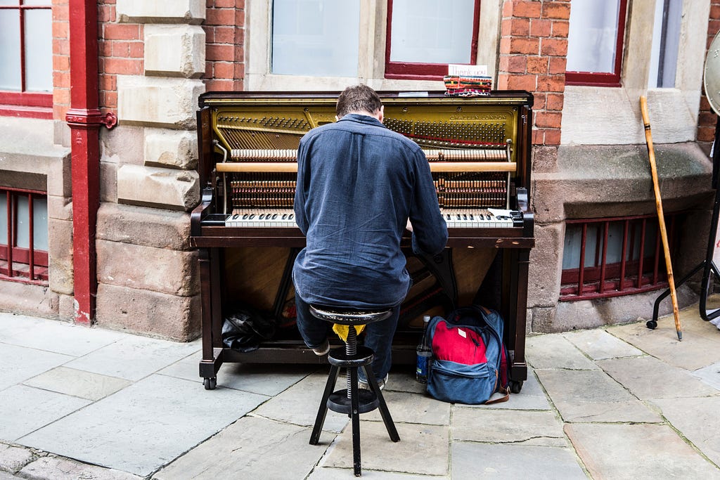 A person plays an opened upright piano on a street corner.