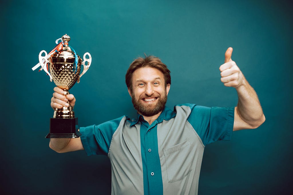 Smiling man holding a trophy and giving the thumbs up.