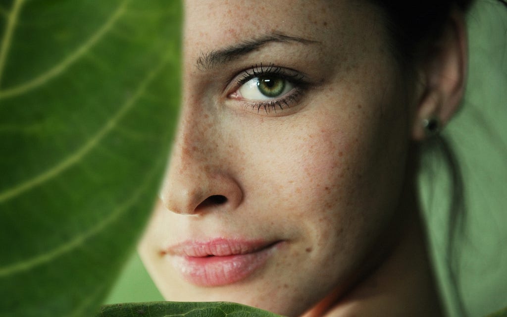 A woman’s face, half-obscured by a large green leaf.