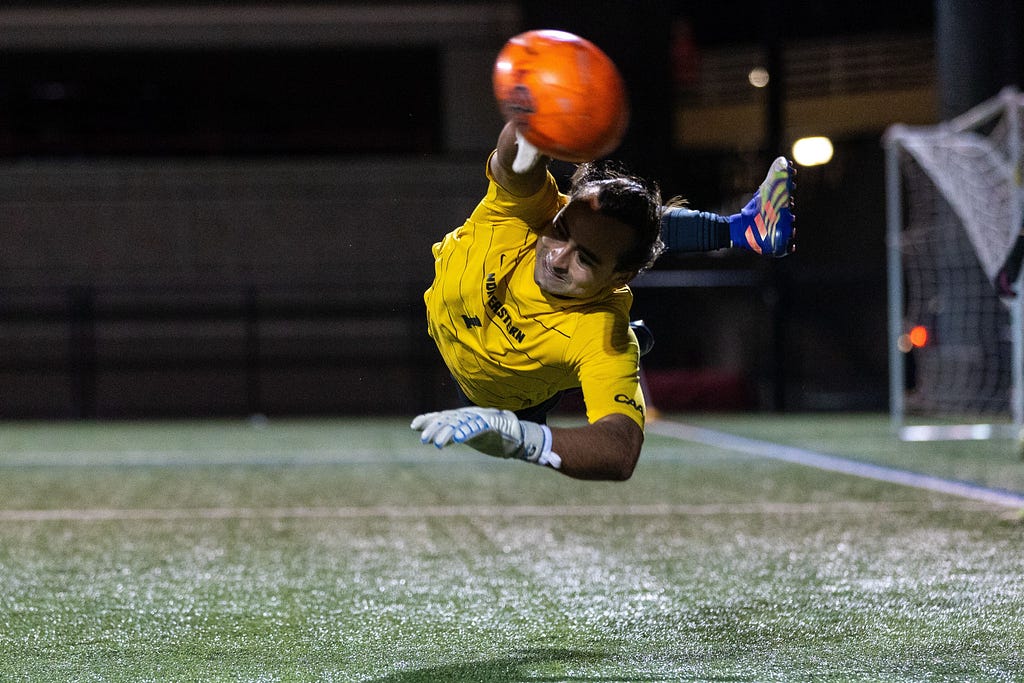 Action shot of Lucas Espada stopping a soccer ball as the goalie for the Northeastern Club Soccer Team