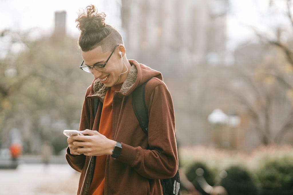 A young man smiling while looking on his mobile phone screen.