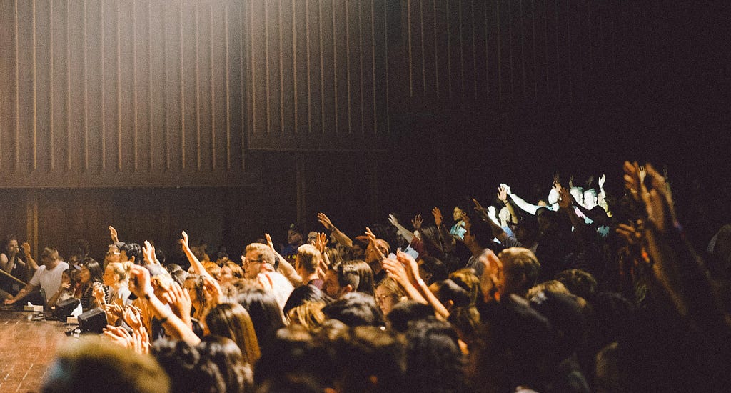 A large audience raising their hands with questions in an auditorium.