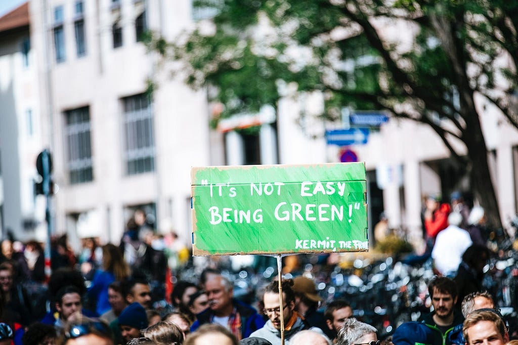 Activist with green climate protest sign which reads, “It’s Not Easy Being Green!” — Kermit the Frog