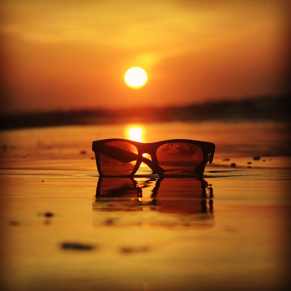 Sunglass on the beach, with the sun setting in the background