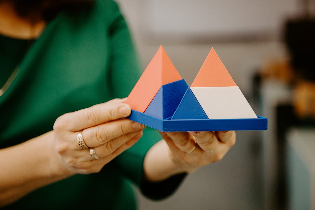 A woman in a green shirt holds two triangles made of blocks.