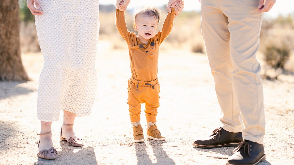 Toddler supported by parents’ hands in desert