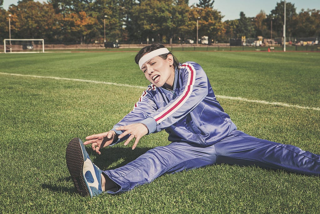 woman stretching on field in a track suit