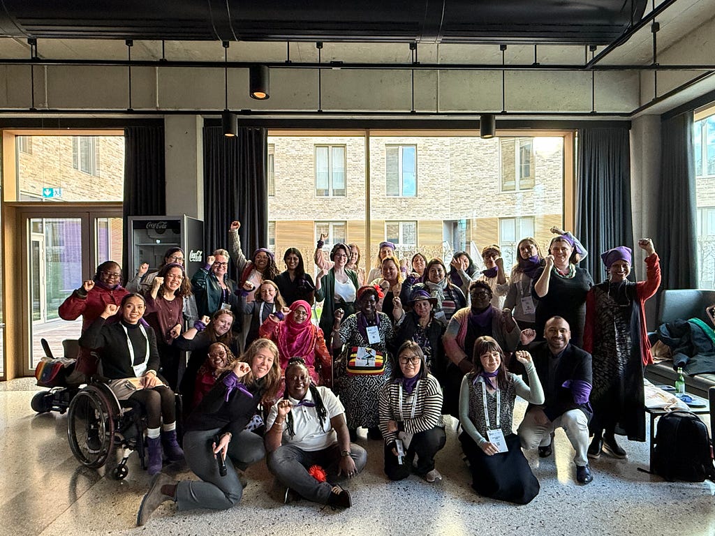 A group of feminists with disabilities and allies at WEI’s Strategy Meeting during the Global Disability Summit in Berlin. Some people are using mobility devices, and some have their fists raised and wearing a purple bandana in solidarity.