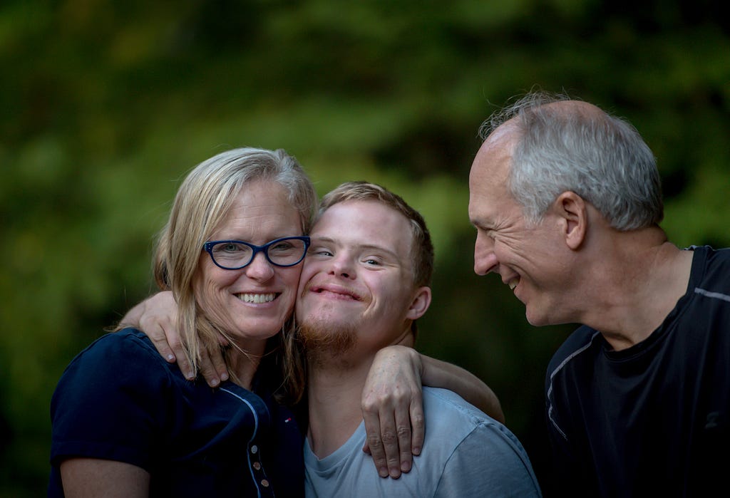 Family embracing a man with down syndrome and smiling to each other.