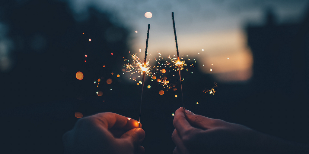 Two hands are holding lit-up sparklers