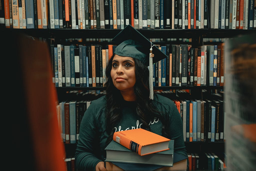 A photo of a female-looking student in a library holding books.
