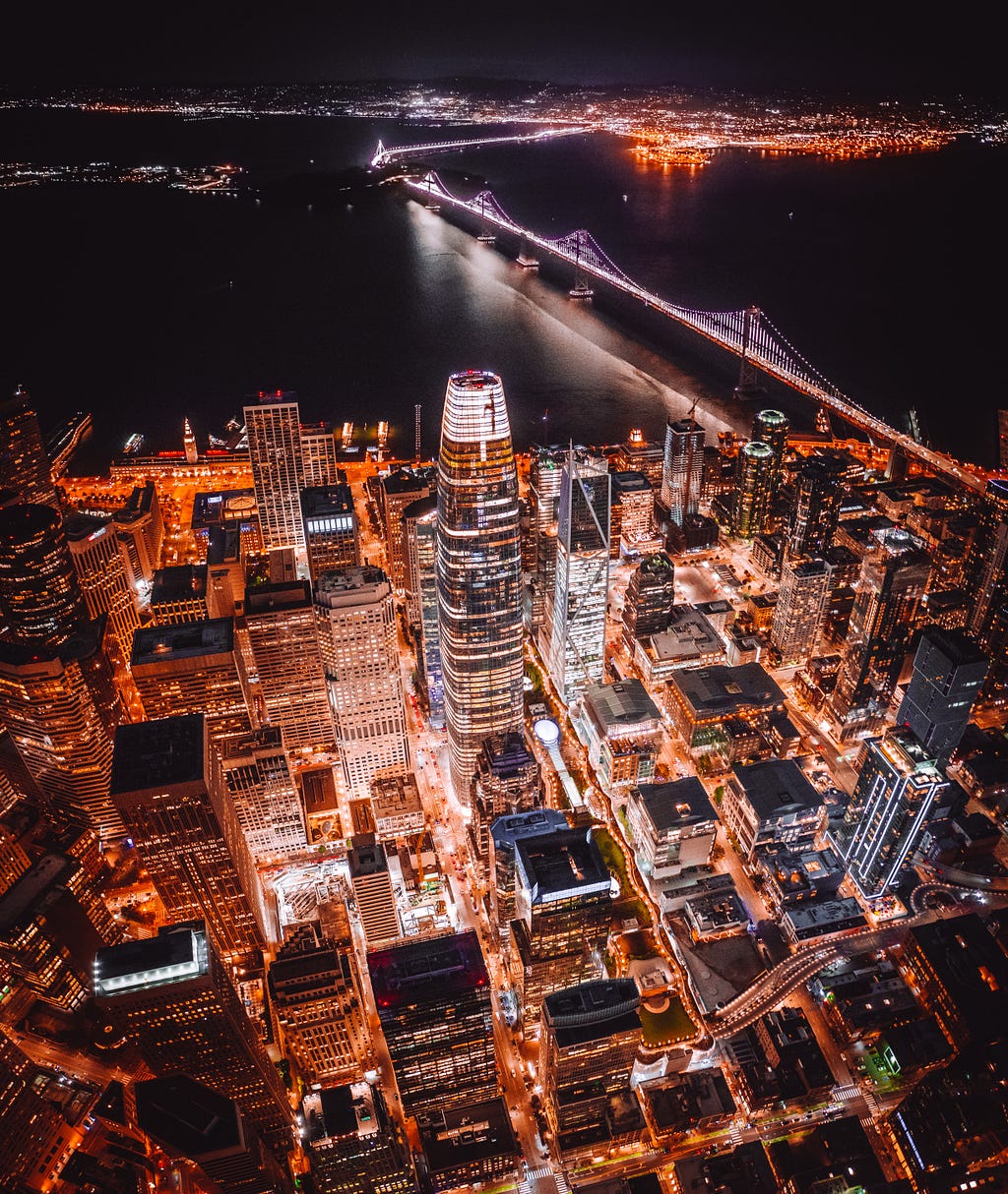 A bird’s eye view of Downtown San Francisco at night. The Salesforce tower is in the center of this evening shot with the Bay Bridge in the background.