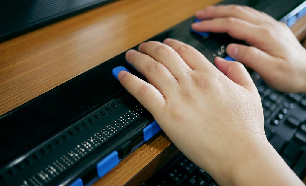 Hands of a person with visual impairment using a braille keyboard.