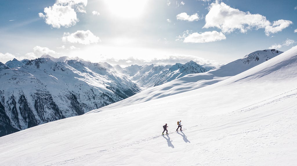 Two skiers climb a snow covered mountain.